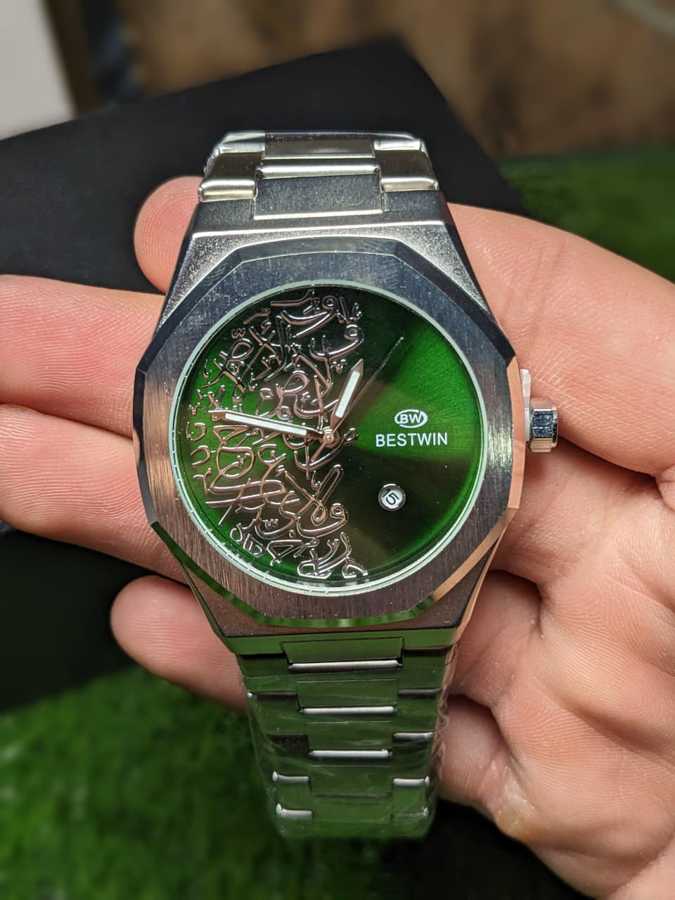 Green dialer and silver watch with intricate design held in a hand