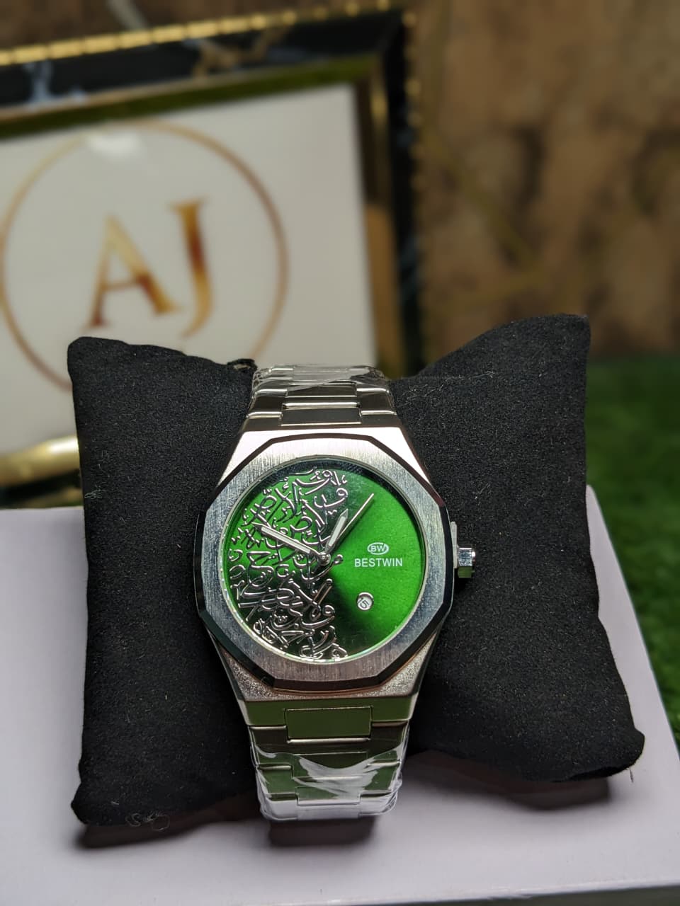Watch with green face and silver case on a black cushion, brand logo in the background