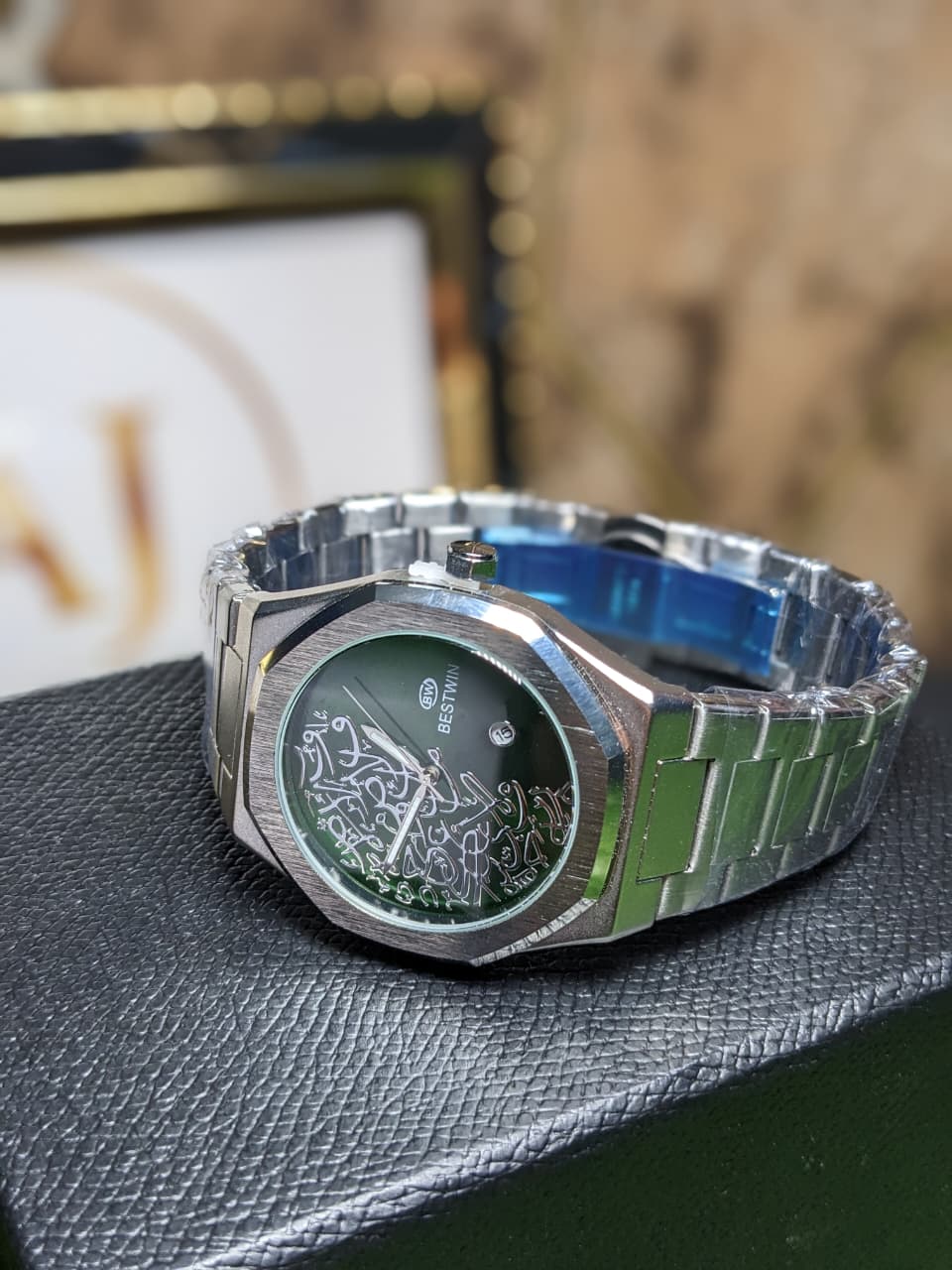 Silver watch with green face and band on a textured surface