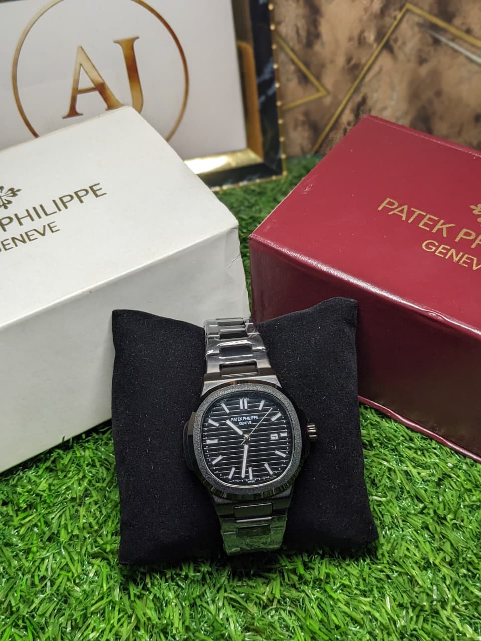 Watch on a black cushion with Patek Philippe and Philippe Geneve boxes in the background.