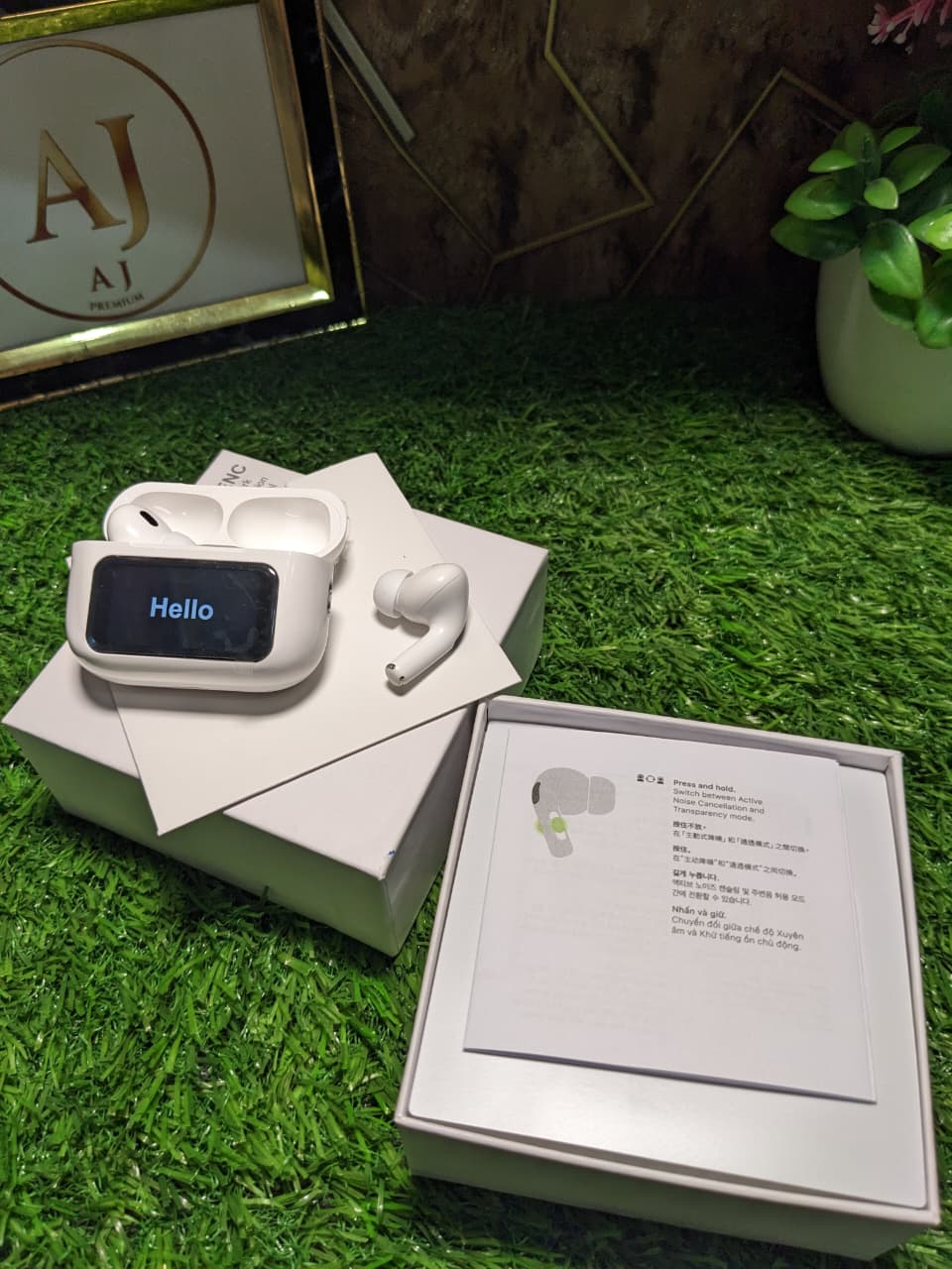 White Earbuds A9 pro with 'Hello' display on a white box on green with AJ premium frame in back