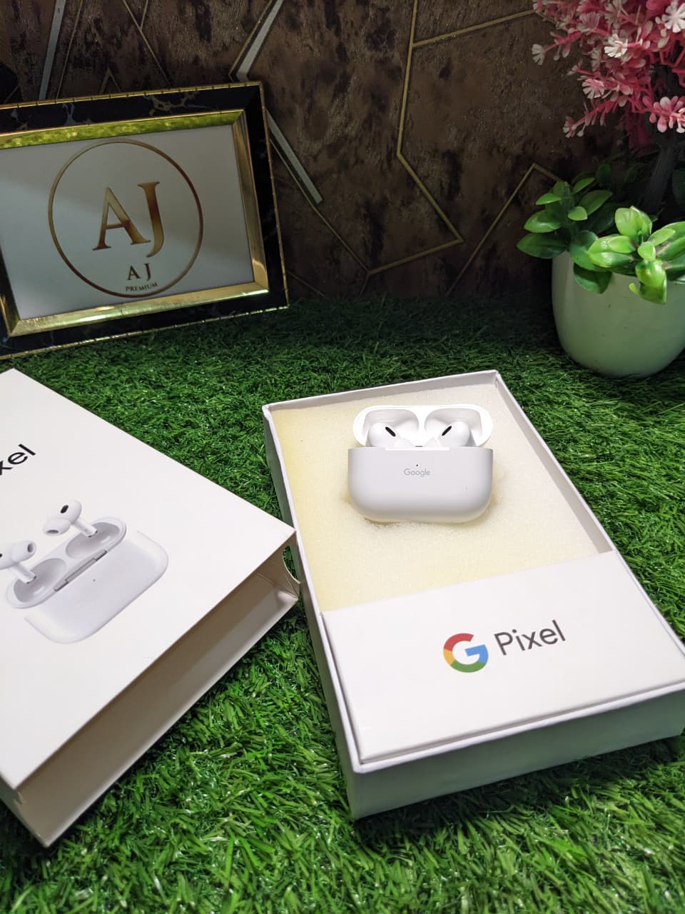 Pixel wireless earbuds in a box on a grass-like surface with decorative elements.