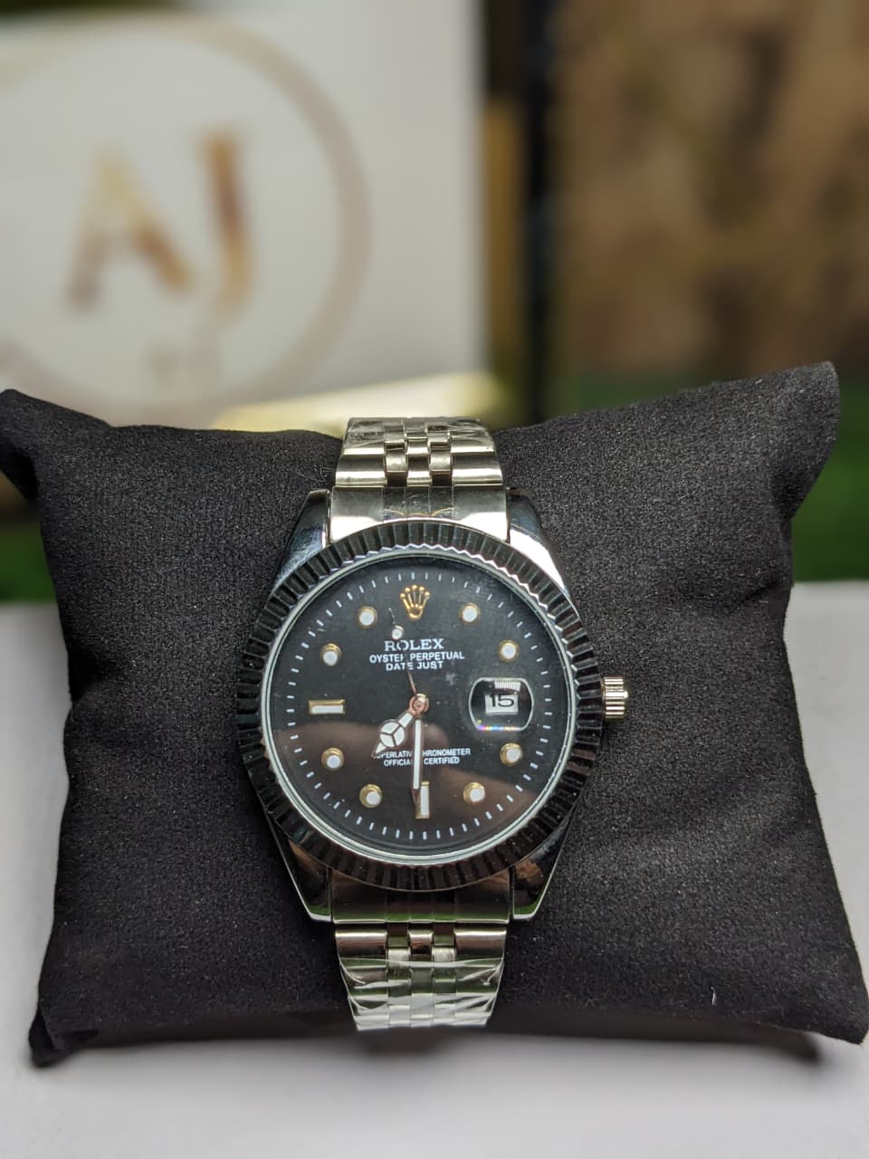 Silver luxury rolex watch with black dial on a black cushion, blurred background