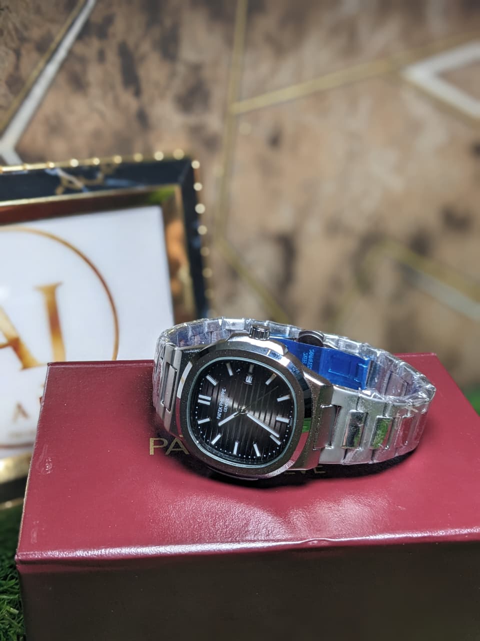 Silver watch with a clear strap on a red box with 'Patek' branding, blurred background