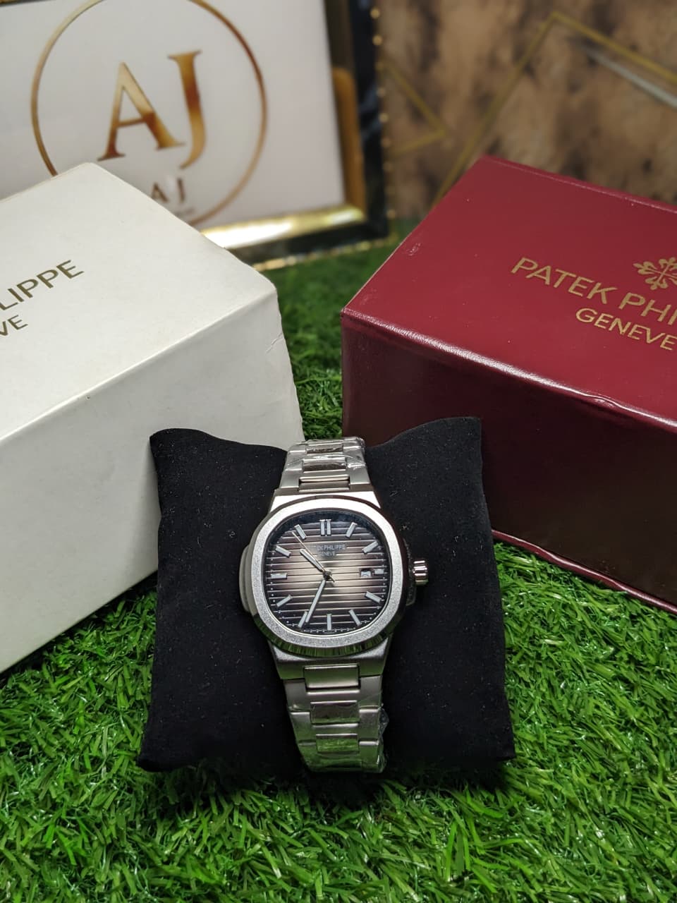 Silver watch on a black cushion with Patek Philippe box in the background
