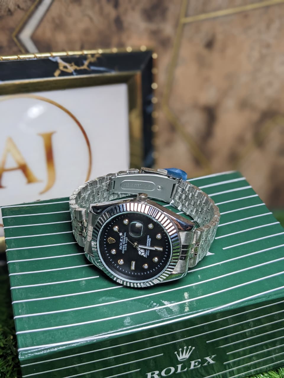 Silver  luxury rolex watch with black face on a green box with Rolex branding