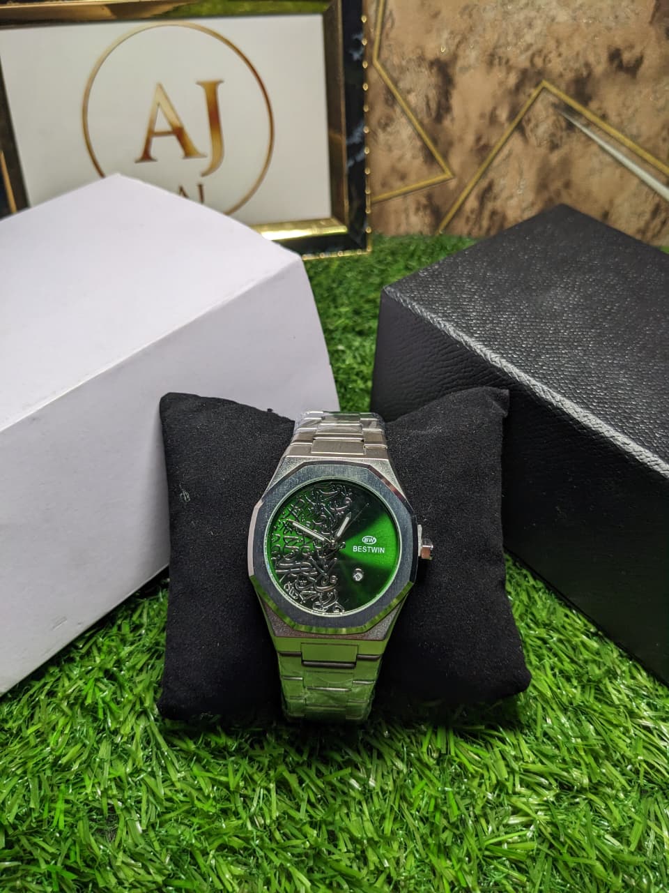 Silver watch with green face dial  on a black cushion, brand box in the background