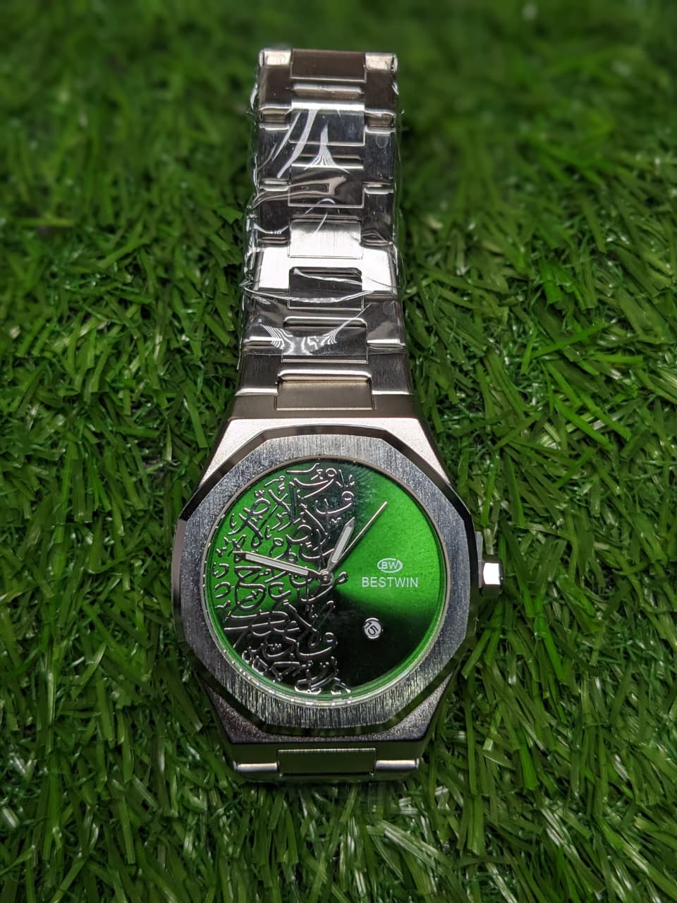 Silver luxury watch with green face on a grass background
